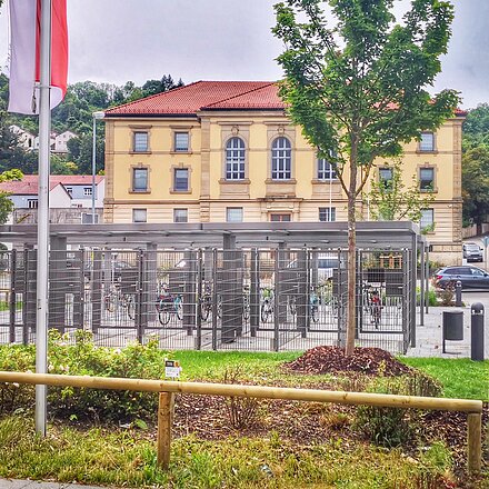 Fahrradboxen vor der Abschiebehaft mit zwei Bäumen und der Stadtfahne