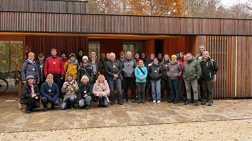 Etwa 30 Naturparkführer stehen vor dem Holzgebäude des Walderlebniszentrums in Schernfeld