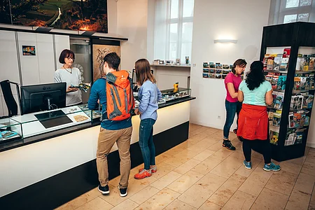 Informationszentrum Naturpark Altmühltal An der Tourist-Information steht ein Pärchen und lässt sich von einer Mitarbeiterin mit halblangen Haaren beraten. Zwei Frauen stehen rechts interessiert am gefülltem Prospektständer.