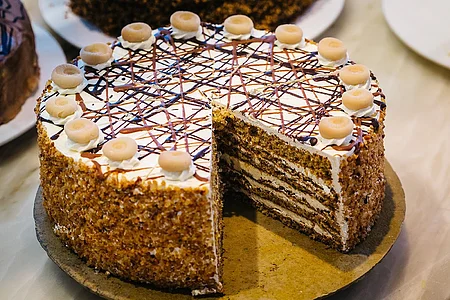 Eine mehrschichtige Torte mit Sahne, Schokoladendekor und Marzipanverzierung auf einem Tisch. Ein Stück fehlt.