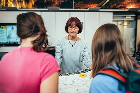 Frau zeigt zwei Personen eine Landkarte in einem Informationsbüro.