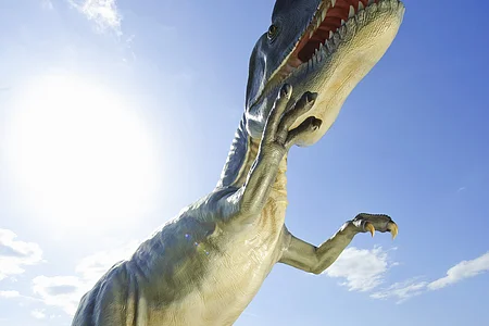 Familie mit zwei Kindern steht vor großem Dinosauriermodell im Freien bei Sonnenschein