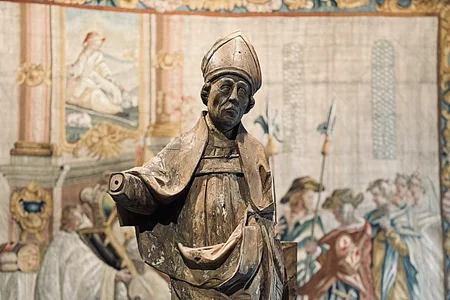 Eine Bischofsstatue steht vor einem verzierten Wandteppich