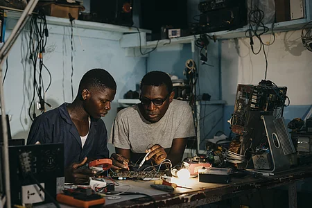 Ausbilder Bertrand Njomko repariert gemeinsam mit Azubi Silas Teyim (19)  ein technisches Geraet.