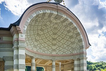 Auf dem Bild ist der mittlere und größte Pavillon des Hofgartens. Der Pavillon ist rund und nach vorne hin geöffnet. Ein Brunnen befindet sich im Zentrum. Dahinter stehen mehrere weiß, grau gemusterte Säulen. Die Kuppel ist innen mit einem mosaikartigen Muster aus grauen und weißen Elementen geschmückt. Das Dach wird von einer vasenähnlichen Figur geziert.
Bildbeschreibung ehemalige Kapuzinerkirche (innen)
